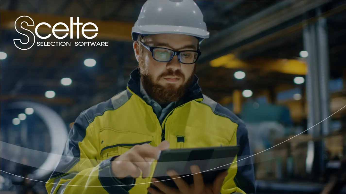 Worker in a high-visibility jacket and safety helmet inspecting data on a tablet inside an industrial facility