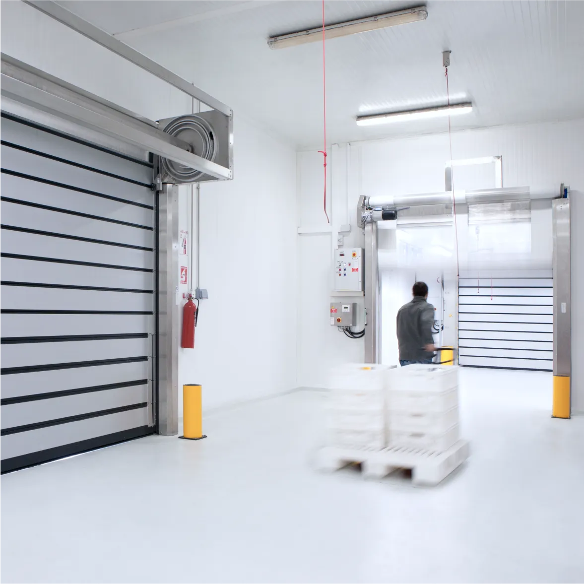 Cold storage facility with high-speed insulated doors and operator moving pallets inside refrigerated warehouse